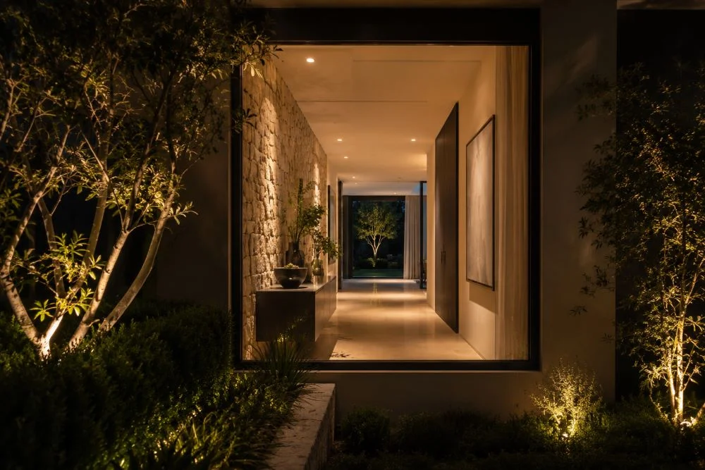 Residential architectural lighting connecting an illuminated hallway with landscape lighting